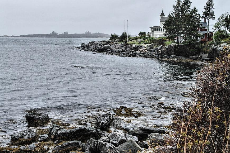 Misty coastal landscape with rocky shoreline and white house