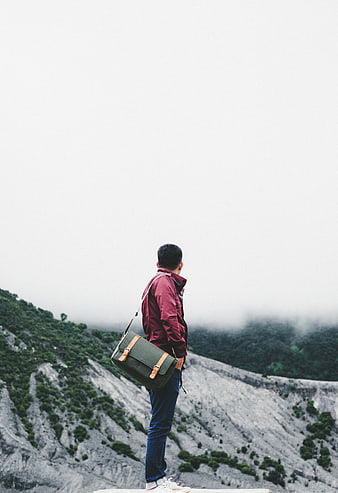 Man with Messenger Bag Standing on Cliff Edge in Foggy Mountains