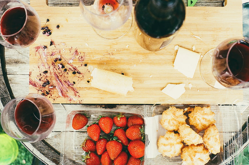 Overhead view of wine, cheese, strawberries, and pastries on a wooden board