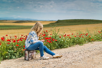 Blonde Woman Sitting on Vintage Suitcase in Poppy Field