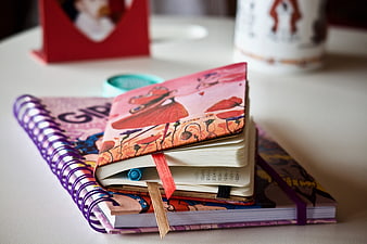 Colorful spiral notebooks and journals stacked on a white desk