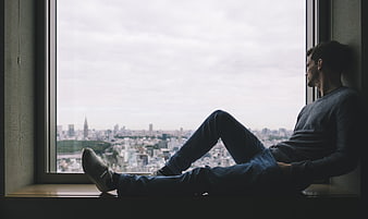 Man sitting on window sill looking at city skyline
