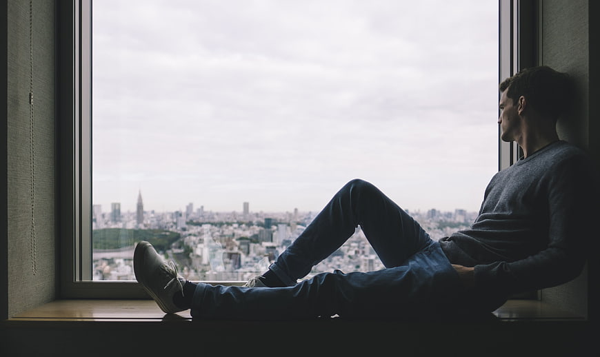 Man sitting on window sill looking at city skyline