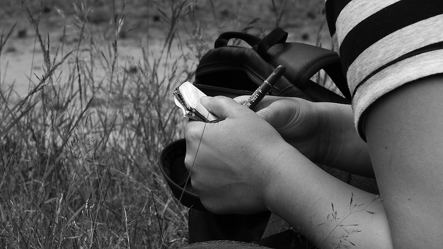 Close-up of hands writing in a notebook outdoors in black and white