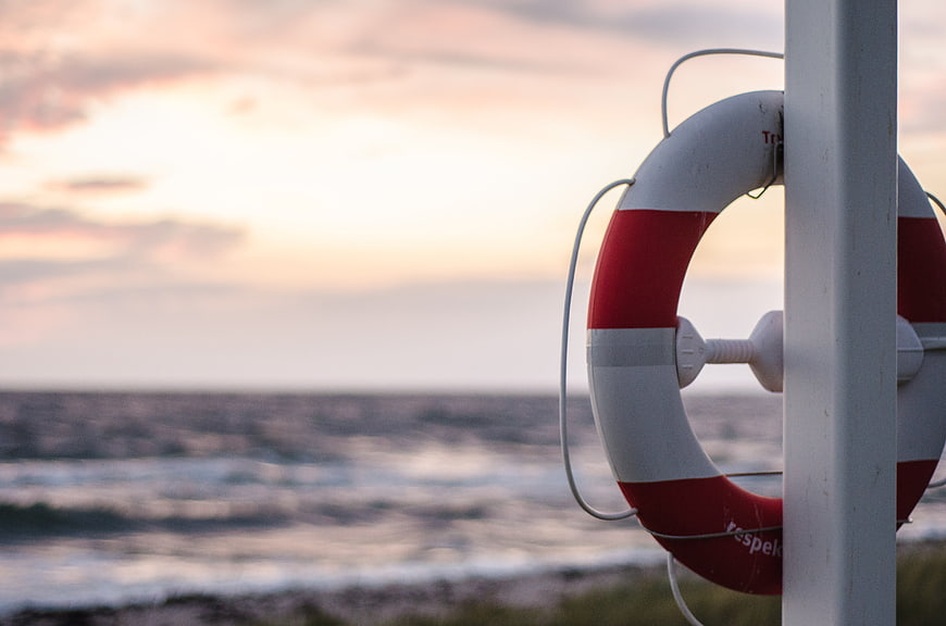 Red and white lifebuoy on a pole against a sunset ocean background