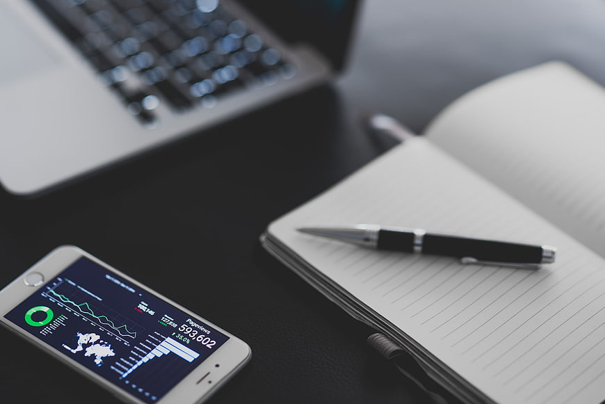 Smartphone Analytics Dashboard on Desk with Laptop and Notepad