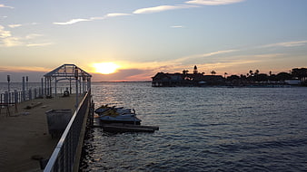 Sunset over a waterfront pier with jet skis and a stilted building