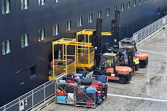 Forklifts loading luggage onto a large cruise ship at the dock