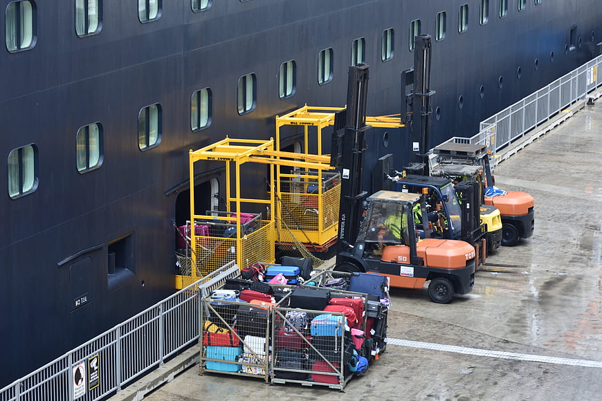 Forklifts loading luggage onto a large cruise ship at the dock
