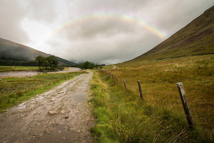 Faint Rainbow Over Muddy Highland Road and Green Hills