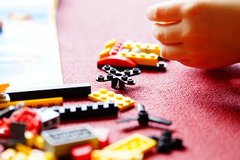 Child's Hand Playing With Colorful Building Blocks On Red Surface