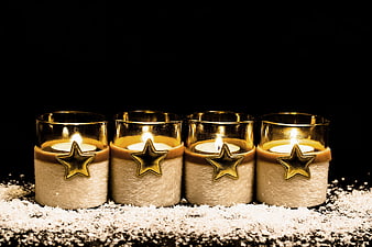 Four lit gold star candles on snow for Christmas