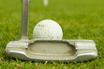 Close-up of golf putter and ball on green grass