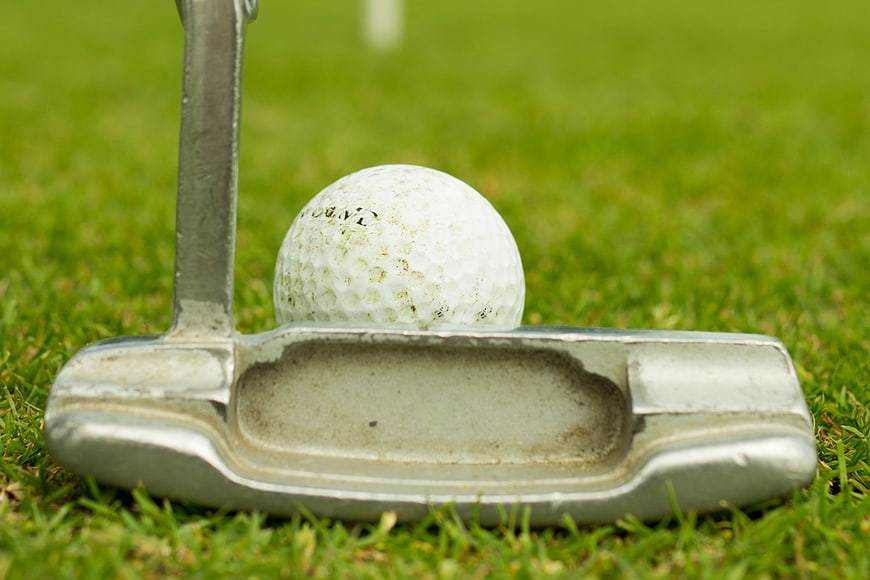 Close-up of golf putter and ball on green grass