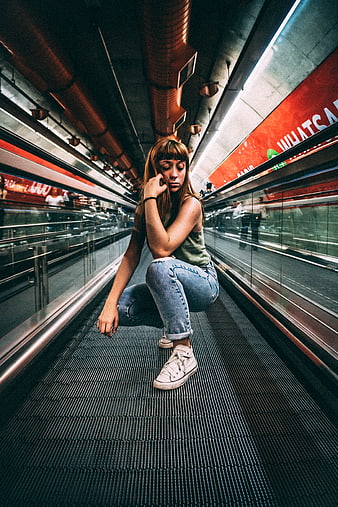 Young woman crouching on moving walkway in subway station