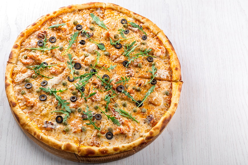 Delicious seafood pizza with olives and arugula on wooden board