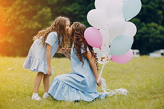 Mother and daughter kissing in a grassy field with pastel balloons