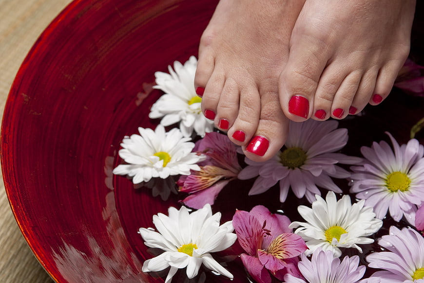 Woman's feet with red pedicure in spa bowl with flowers