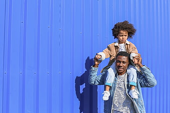 Father carrying child on shoulders against blue wall