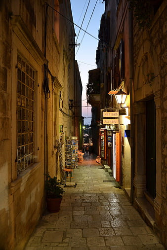 Narrow cobblestone alley in old town at dusk with warm street lights