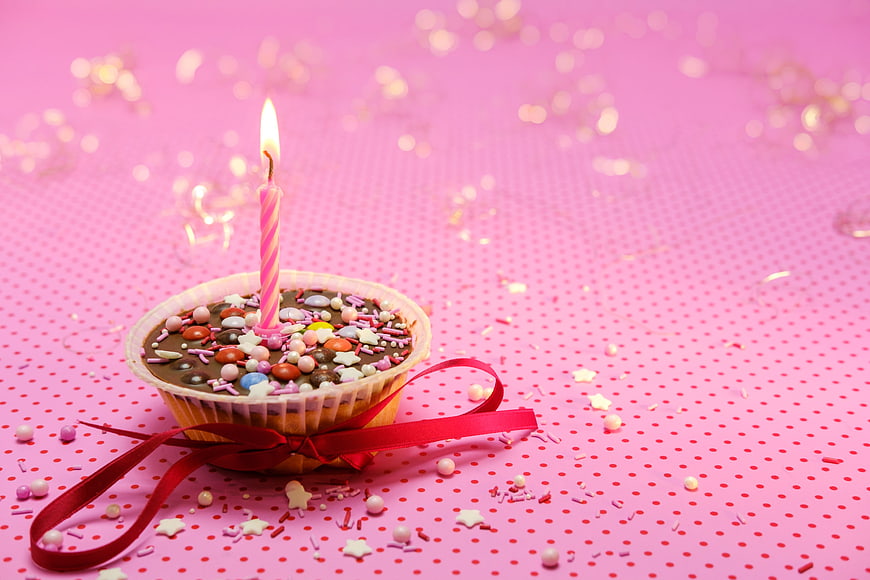 Birthday Muffin With Candle And Red Ribbon On Pink Background