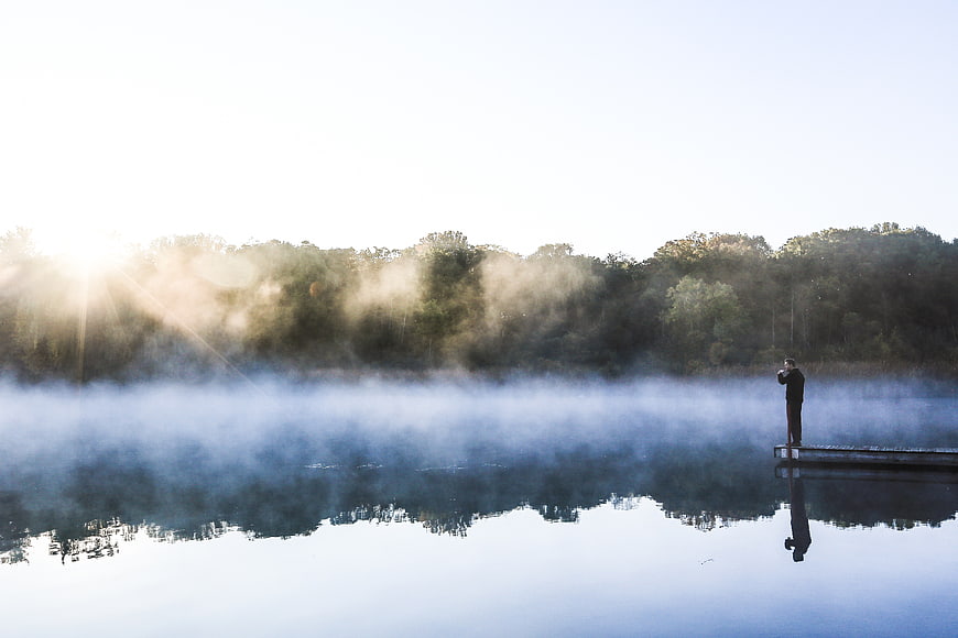 Man standing on dock in misty lake at sunrise
