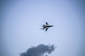 F-16 fighter jet flying in blue sky with smoke trail