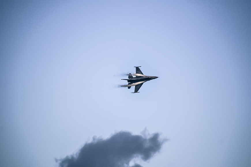 F-16 fighter jet flying in blue sky with smoke trail