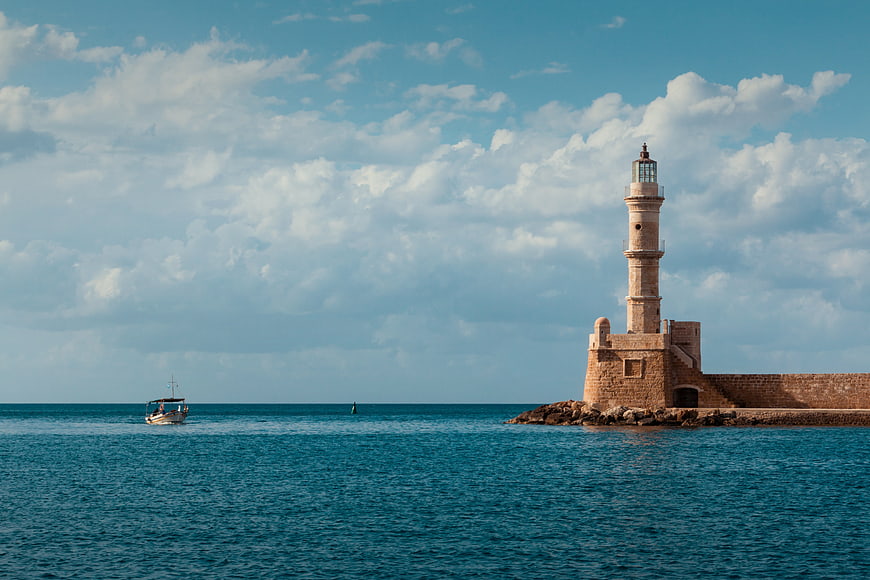 Historic stone lighthouse on a breakwater with a fishing boat in the sea