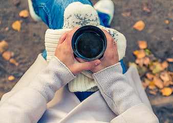 First-person view of hands holding a black mug in autumn