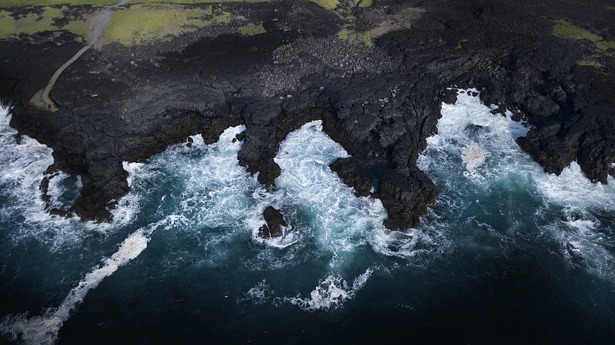 Aerial view of dramatic black volcanic cliffs meeting crashing ocean waves