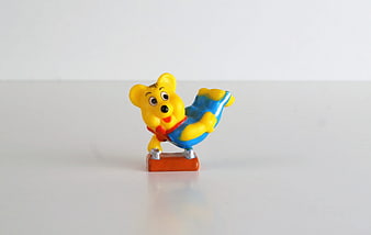 Yellow plastic bear figurine in blue overalls on white background