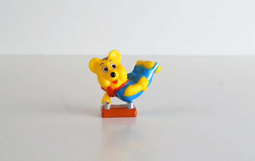 Yellow plastic bear figurine in blue overalls on white background