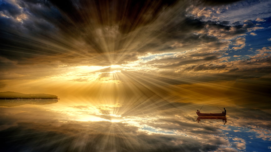 Dramatic sunset sunbeams over calm lake with small fishing boat