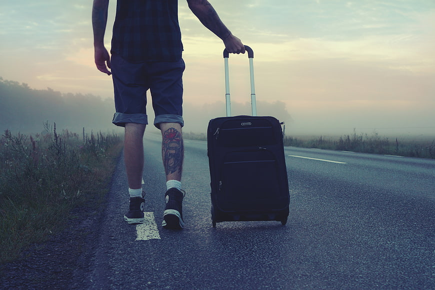 Man with suitcase hitchhiking on foggy road at sunrise