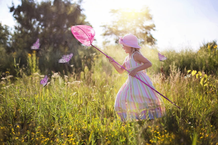 Little girl in pink dress chasing butterflies in a sunny wildflower meadow