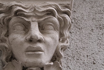 Close-up of weathered stone face sculpture on building facade