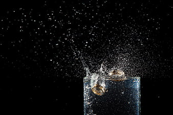 Gold wedding rings splashing into water on black background