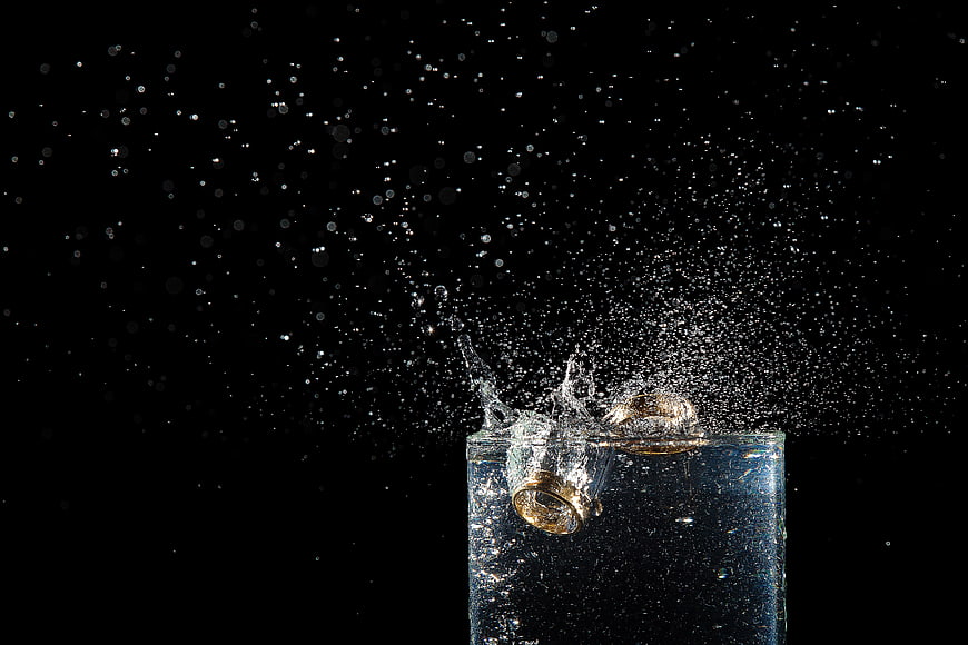 Gold wedding rings splashing into water on black background
