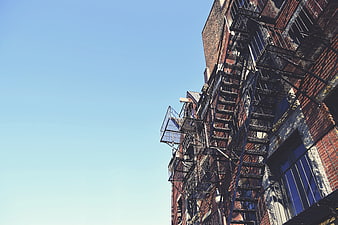 Low angle view of brick building with fire escape against blue sky