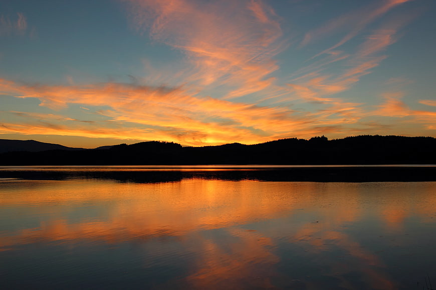 Vibrant Orange Sunset Reflection on Calm Lake with Mountain Silhouette