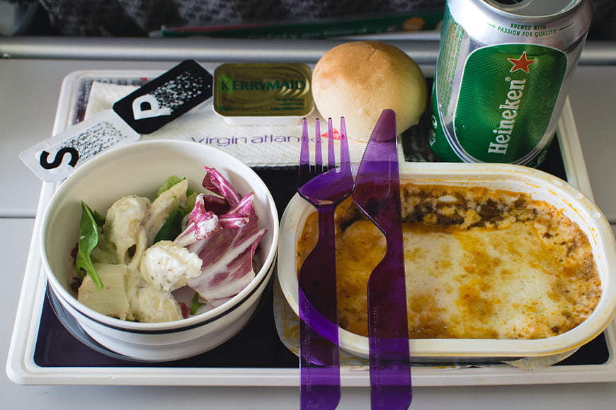 Airplane meal tray with salad, pasta, bread, and beer