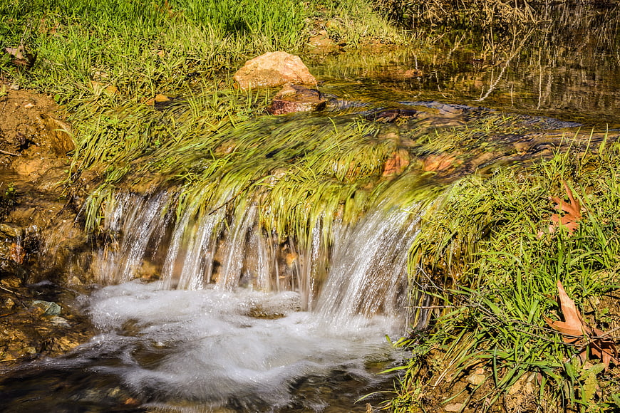 Small waterfall cascading over grassy bank in a stream