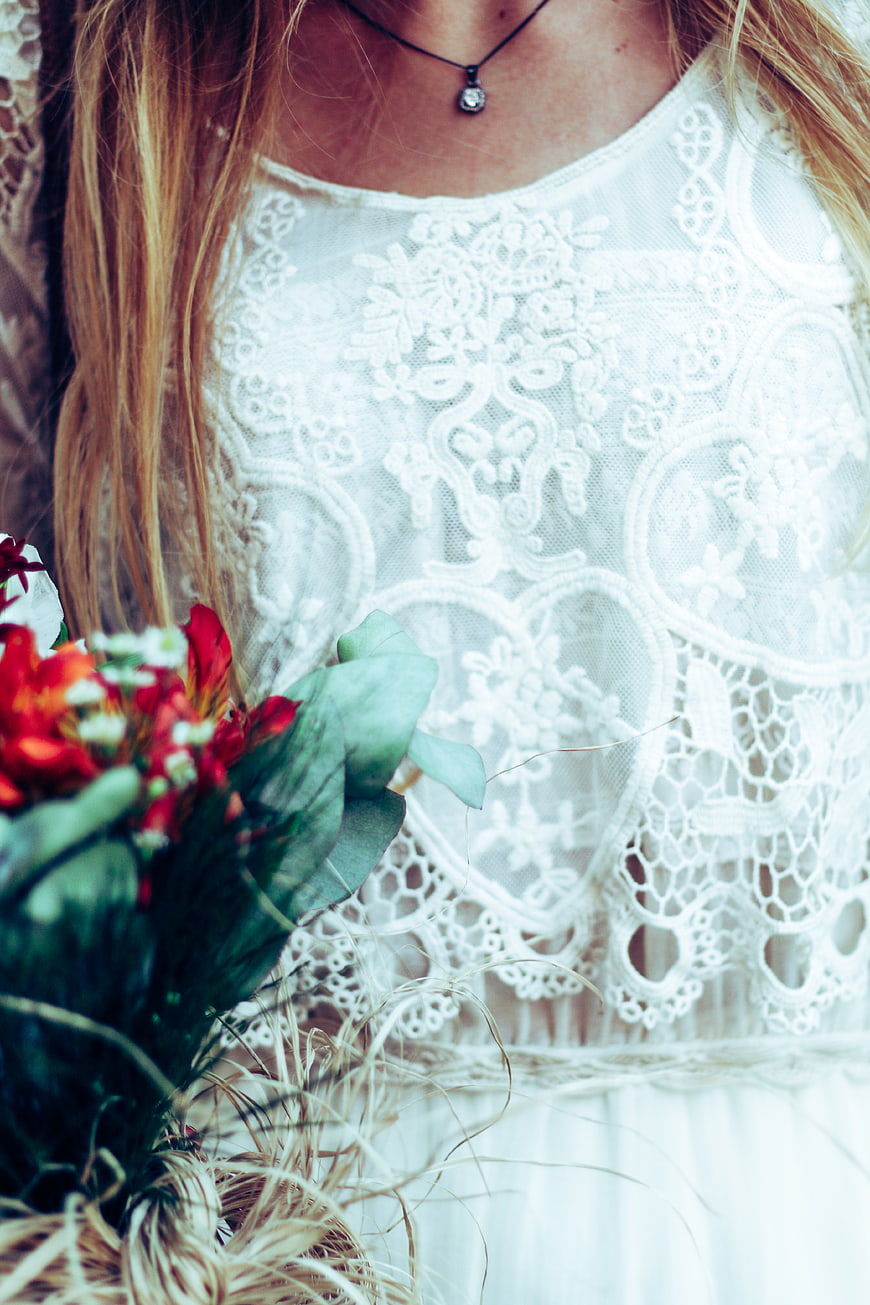 Close-up of woman in white lace dress holding red flowers