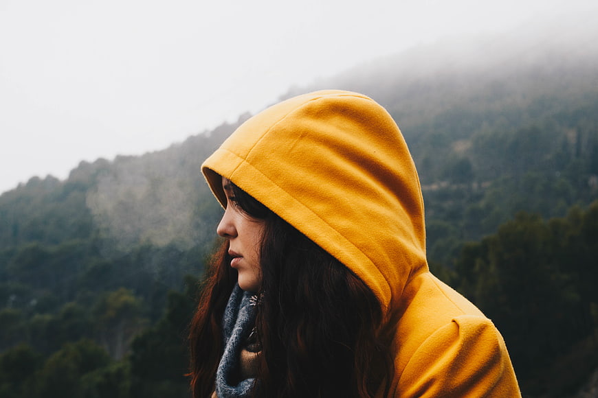 Woman in yellow hoodie looking at foggy mountain landscape