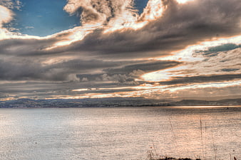 Dramatic sunset clouds over calm sea with distant coastline