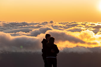 Silhouette of couple embracing above clouds at sunset