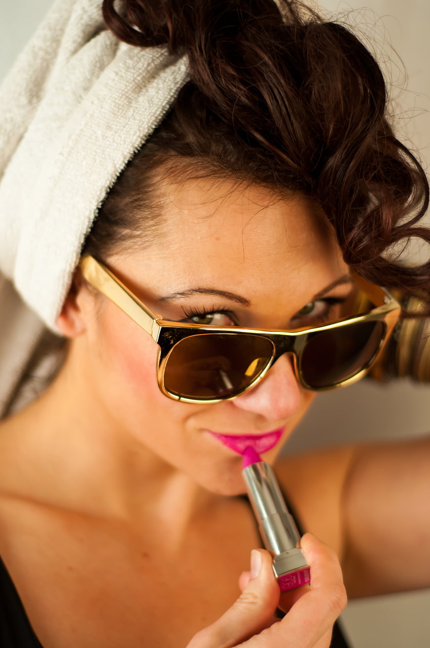 Woman applying pink lipstick with sunglasses and towel
