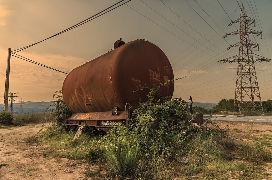 Rusty abandoned train tanker car in overgrown field
