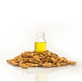 Almond oil bottle surrounded by raw almonds on white background